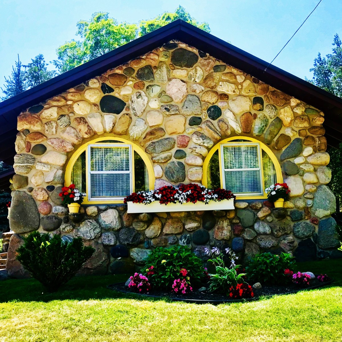 Stone house with curved windows and colorful flowers in window boxes and garden.