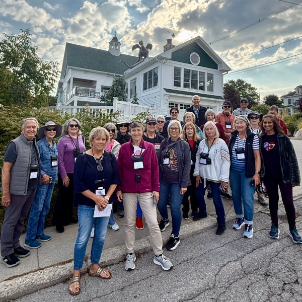 Group of people posing outside a large house under a cloudy sky.