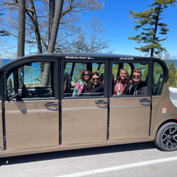 Four people smiling inside a beige electric tour vehicle by a scenic lakeside.