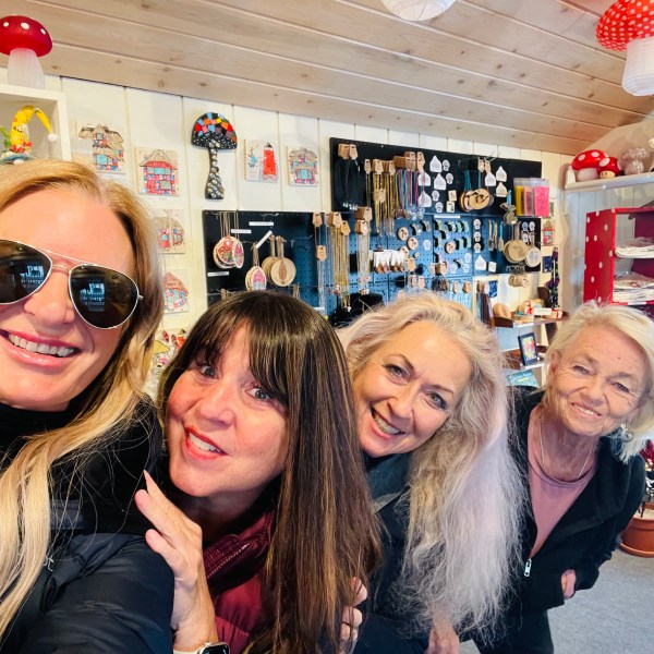 Four women smiling inside a shop with colorful decor and souvenirs.
