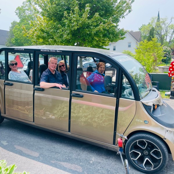 Four people inside a gold electric shuttle parked on a sunny street.
