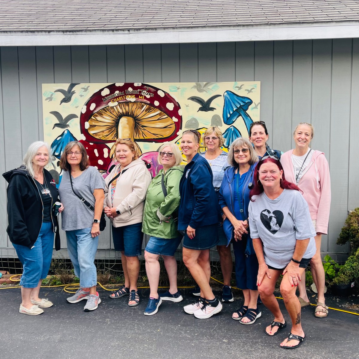 Group of women posing in front of a mural with colorful mushrooms and birds.