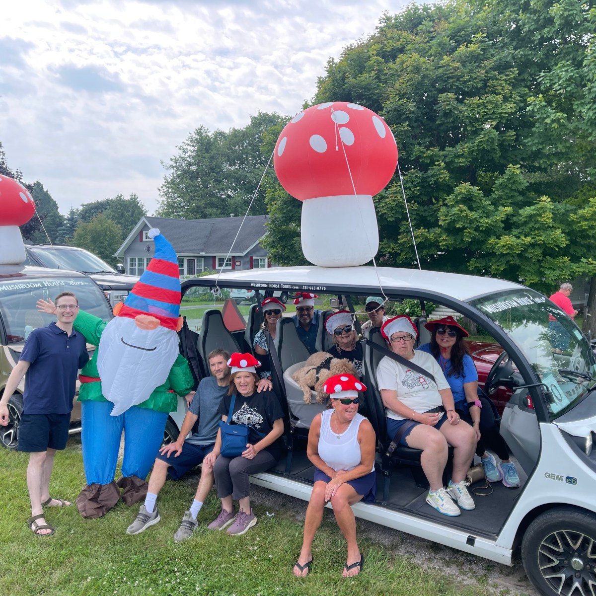 People in mushroom hats and a gnome costume by a vehicle with large mushroom decorations.