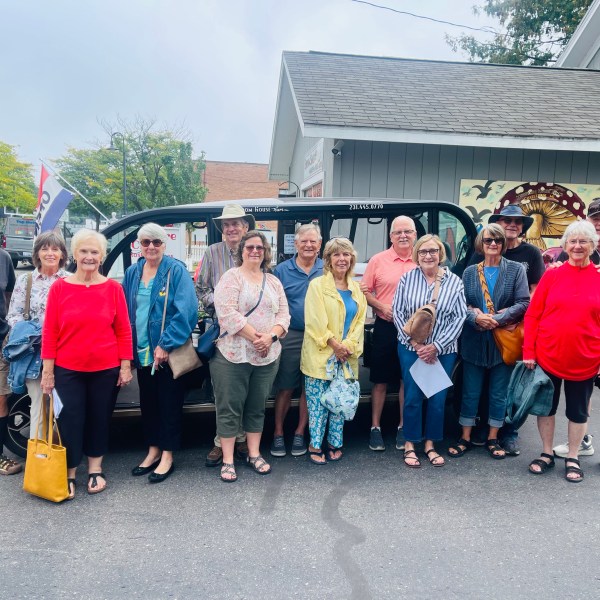 Group of 15 people standing outside a building, smiling at the camera.