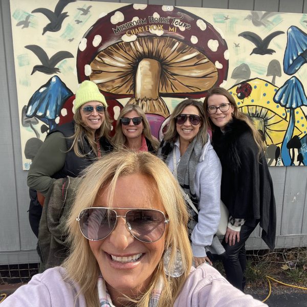 Five women smiling in front of a colorful mushroom mural.