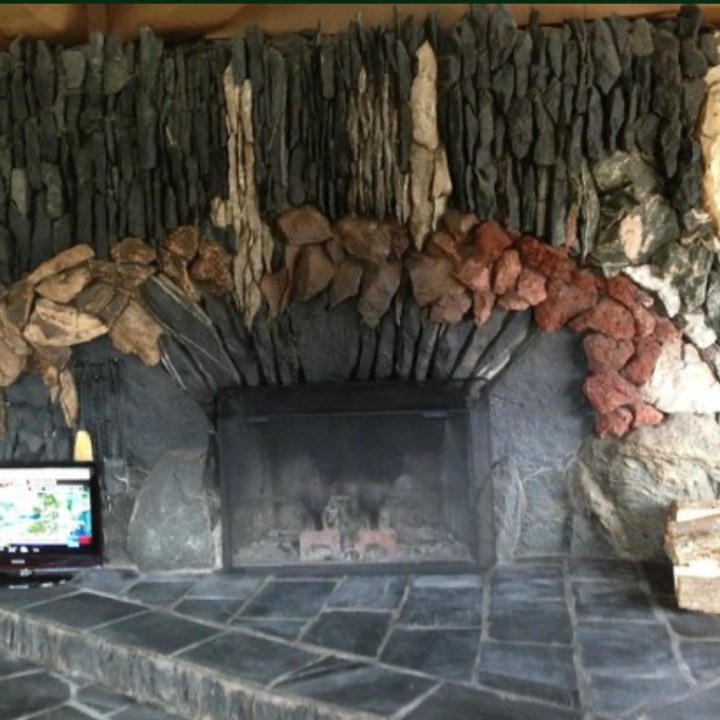 Stone fireplace with colorful rocks, small TV, and wood pile on tiled floor.